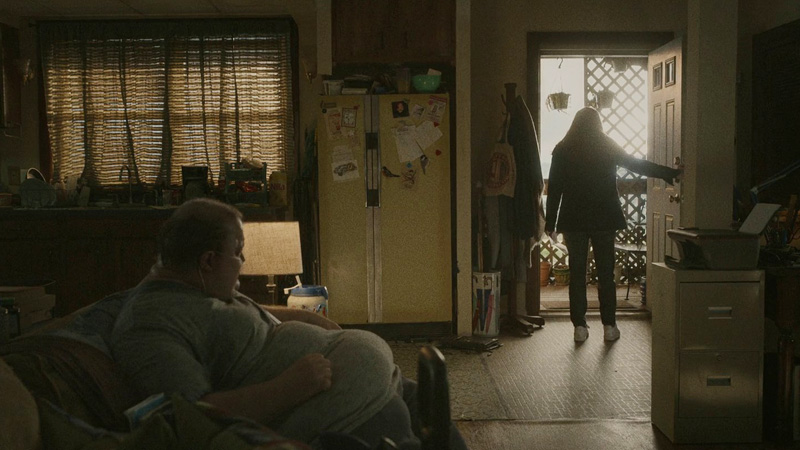 『ザ・ホエール』玄関扉の前に立つエリーとソファに座るチャーリー